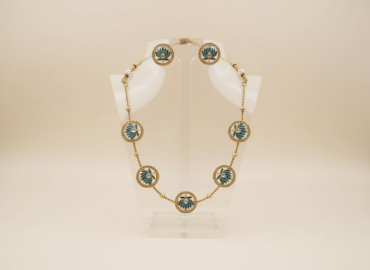 Gold necklace with green accents on a white stand against a beige background