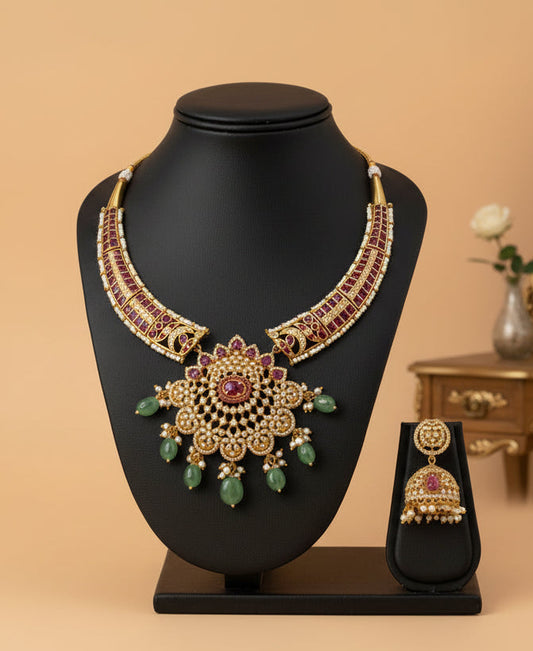 Gold necklace with red and green stones and matching earrings on a white fabric background