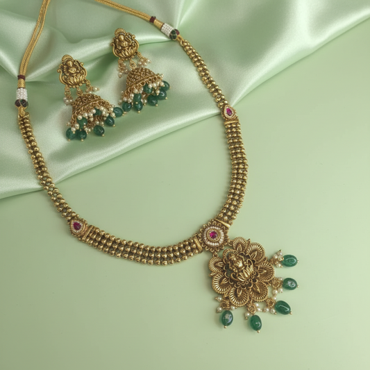 Gold necklace with green gemstones on a light green satin background