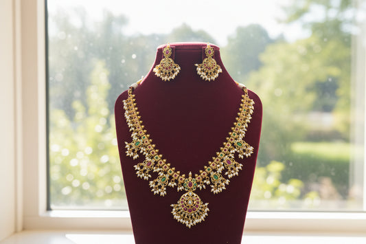 Gold necklace with green and red stones on a maroon stand