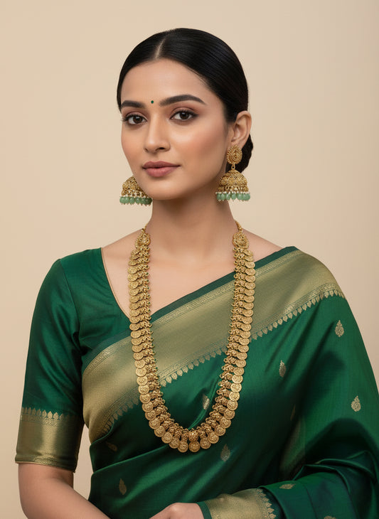 Woman wearing a green saree with gold jewelry against a beige background