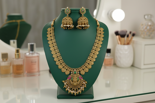 Gold necklace and earrings on a green stand against a green background