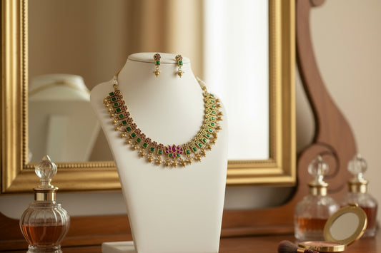 Gold necklace with green and red accents on a mannequin bust against a beige background