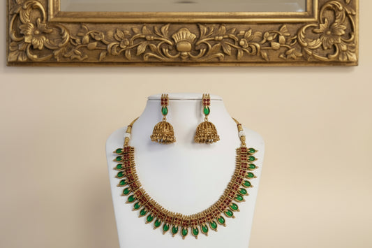 Gold necklace with green stones and matching earrings on a white stand against a beige background