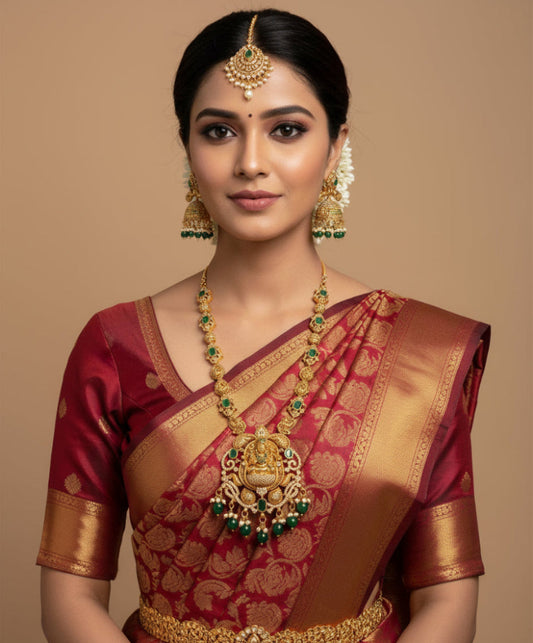 Woman wearing a traditional maroon saree with gold jewelry on a beige background