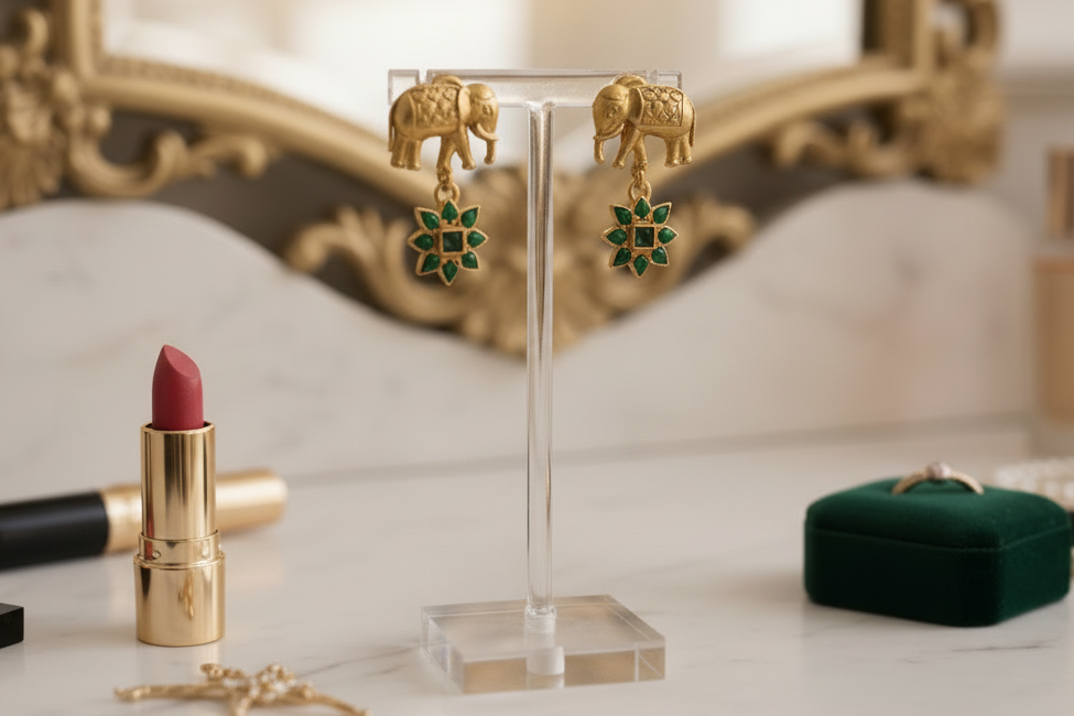 Gold elephant earrings with green gemstones on a light green background