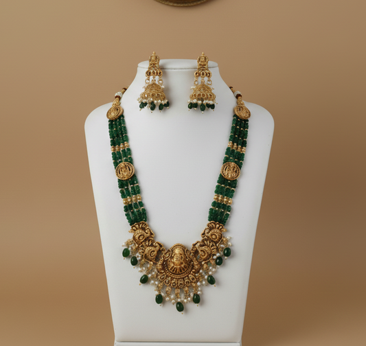 Gold and green beaded necklace set on a mannequin bust against a beige background