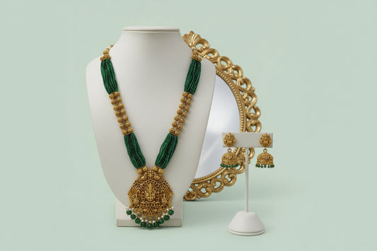 Green and gold necklace with matching earrings on a mannequin and stand against a light green background