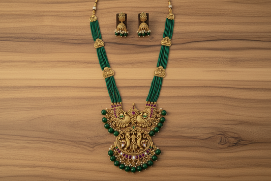 Ornate green and gold necklace with matching earrings on a pink fabric background