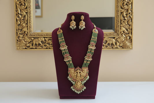 Gold necklace with green and red stones on a white background