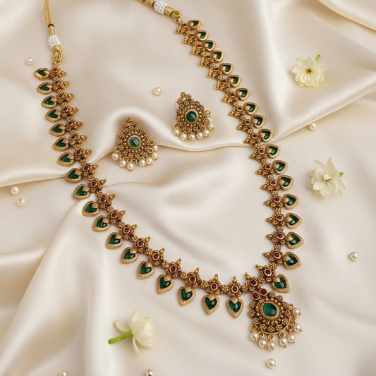 Ornate gold necklace with green gemstones on a satin surface with flowers.