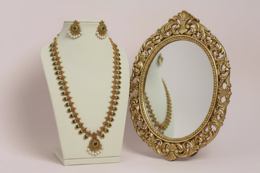 Gold necklace with green gemstones and pearl earrings on a white stand.