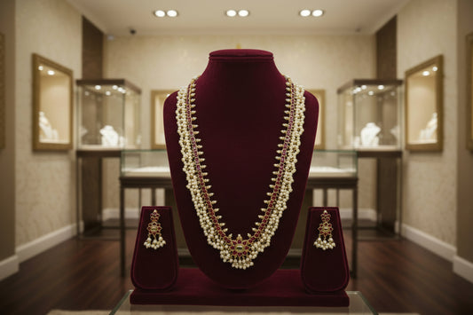 Pearl necklace with red stones and matching earrings on a white mannequin bust against a beige background.