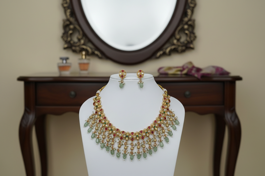 Gold necklace with green and red stones on a mannequin against a cream background
