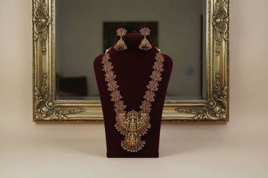 Ornate gold necklace with pink stones on a white stand against a pink background