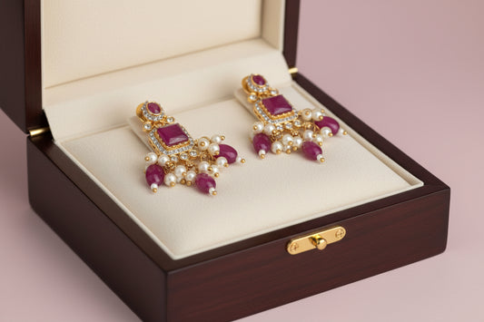 Pair of gold earrings with red stones and pearls on a gold stand against a gray background