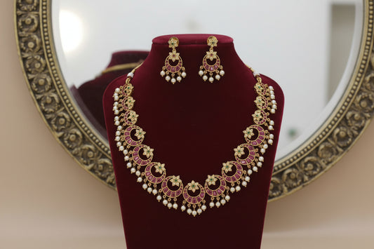 Ornate necklace and earrings set on a red velvet stand with a beige background