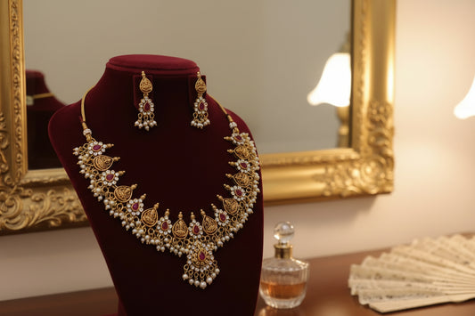 Gold necklace with red and white stones on a red velvet stand against a gray background