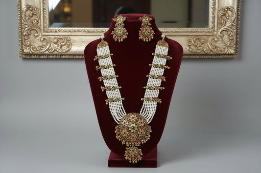 Ornate necklace and earrings on a gold stand against a gray background