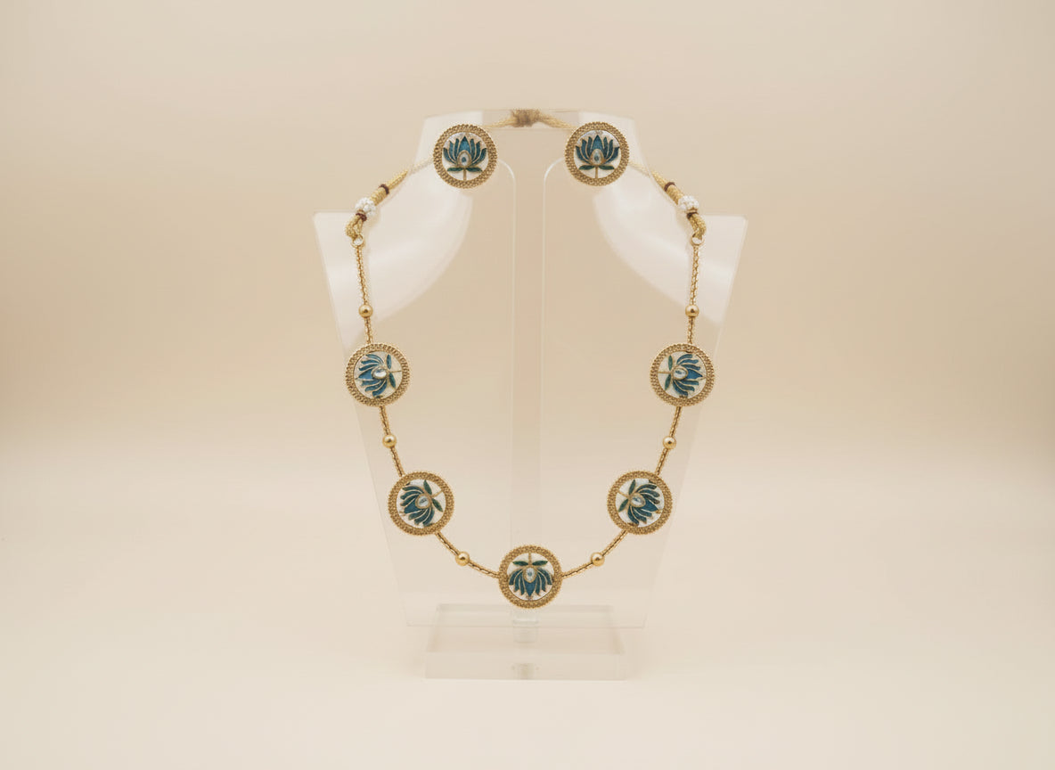 Gold necklace with green accents on a white stand against a beige background