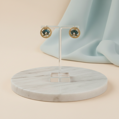 Gold earrings on a clear stand with a marble base against a light blue background