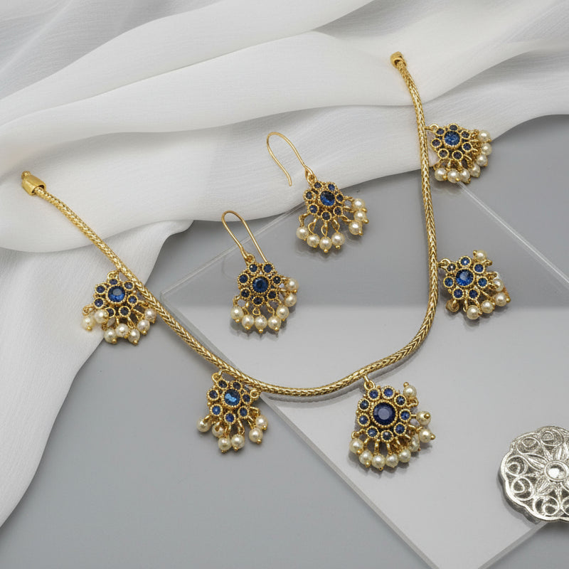 Gold jewelry set with pearls and blue stones on a gray surface