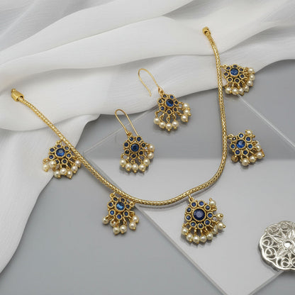Gold jewelry set with pearls and blue stones on a gray surface