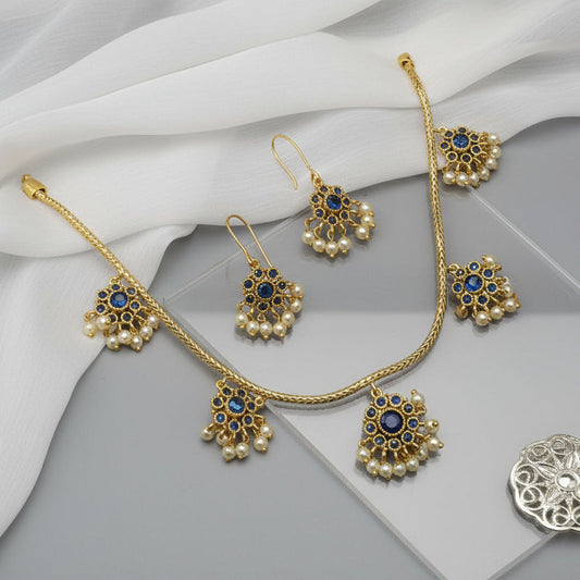 Gold jewelry set with pearls and blue stones on a gray surface