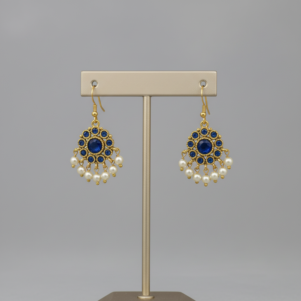 Pair of gold earrings with blue gemstones and pearl accents on a gray background