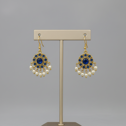 Pair of gold earrings with blue gemstones and pearl accents on a gray background