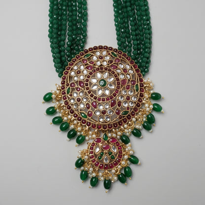 Ornate necklace with green beads and gold and red accents on a gray background