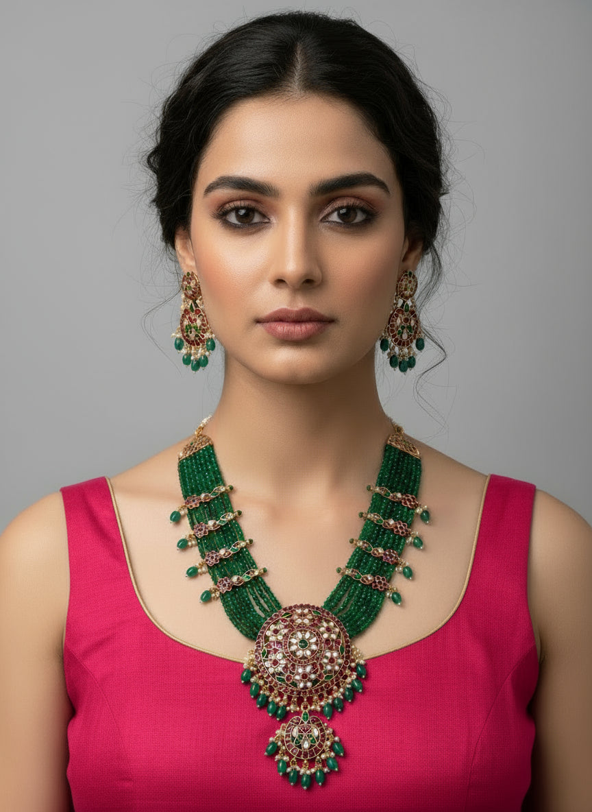 Woman wearing a green and gold necklace with a pink top on a gray background