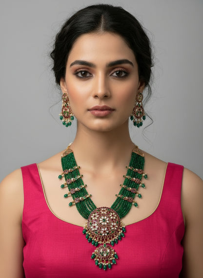 Woman wearing a green and gold necklace with a pink top on a gray background
