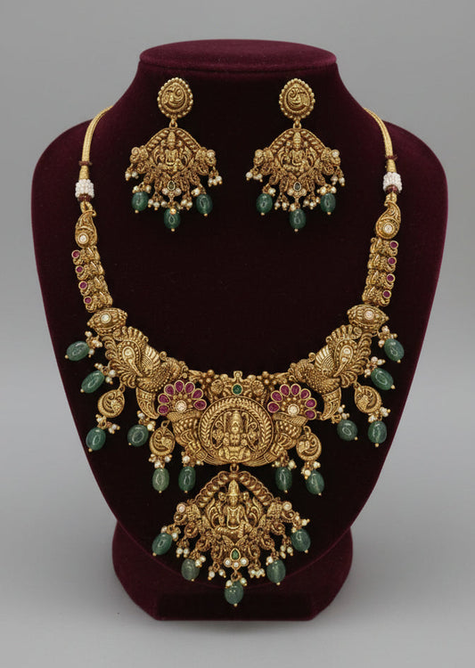 Gold necklace with green beads and matching earrings on a dark red stand.