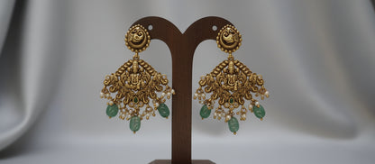 Gold earrings with green stones on a brown stand against a gray background