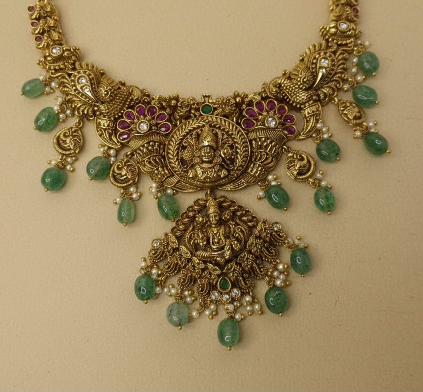 Ornate gold necklace with green gemstones on a beige background
