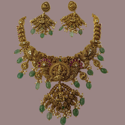 Gold necklace with green gemstones and matching earrings on a brown background