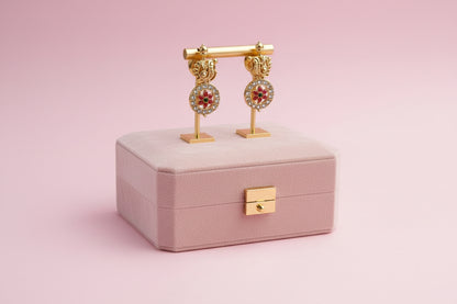 Gold earrings on a pink jewelry box with a pink background
