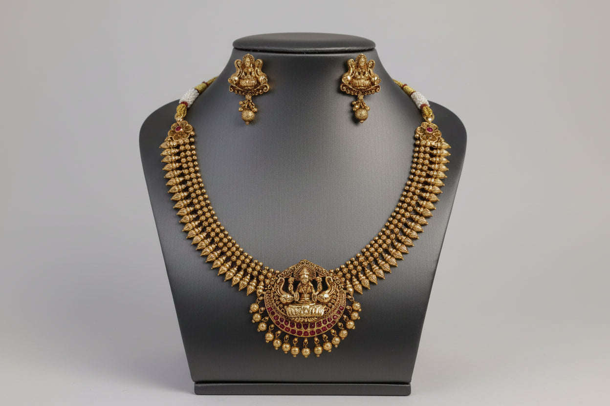 Gold necklace and earrings on a black mannequin against a gray background