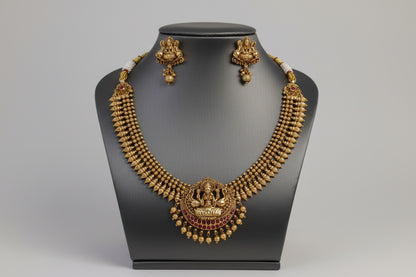 Gold necklace and earrings on a black mannequin against a gray background