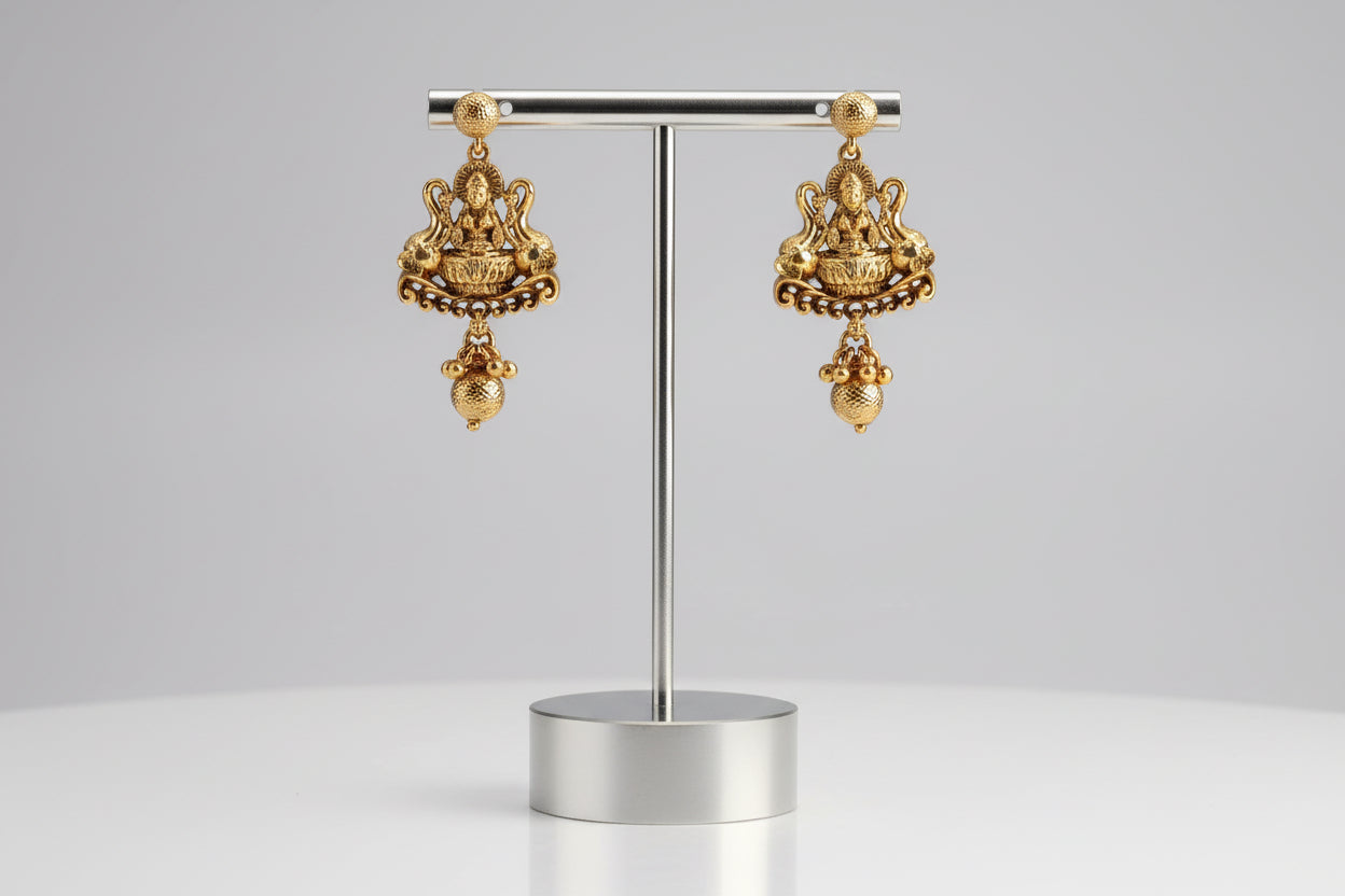Gold earrings held in a hand with a neutral background