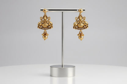 Gold earrings held in a hand with a neutral background