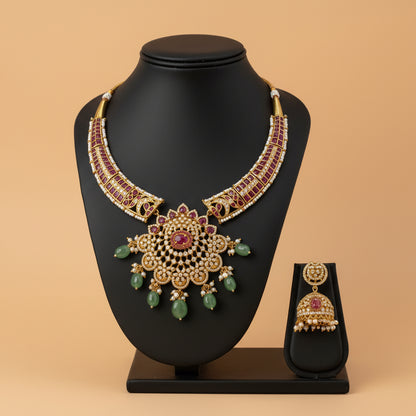 Gold necklace with red and green stones and matching earrings on a white fabric background
