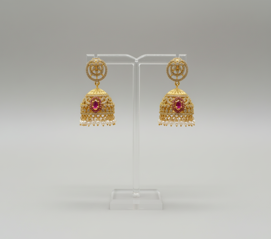 Gold earrings with red gemstones on a clear stand against a pink background