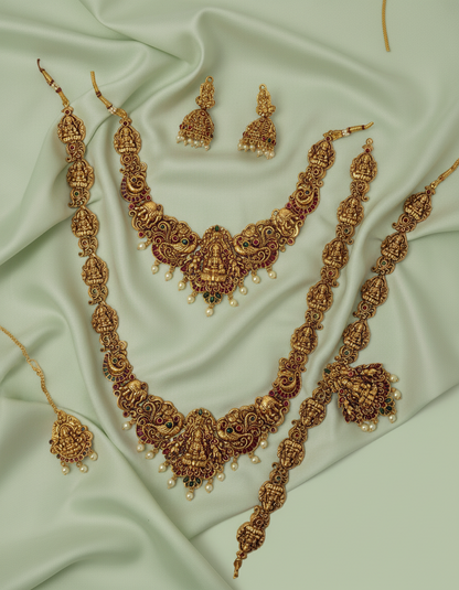 Ornate gold necklace set with earrings on a light green fabric background