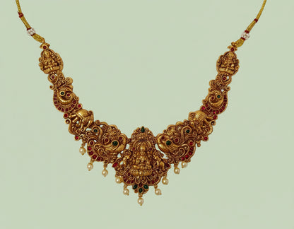 Ornate gold necklace with red and green stones on a light green background