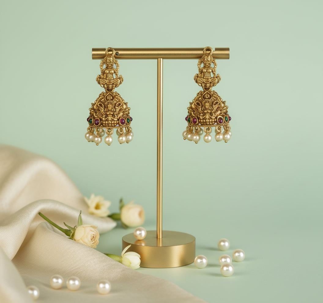 Gold earrings on a gold stand with pearls and flowers on a light green background