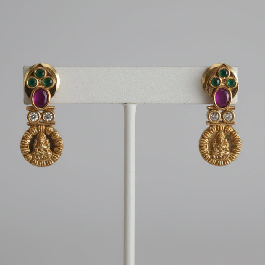 Gold earrings with gemstones on a white fabric background