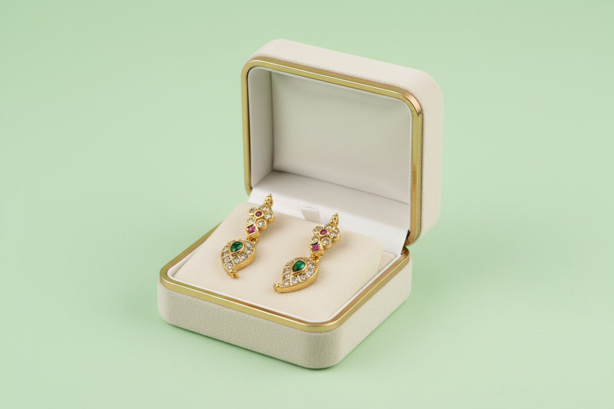 Gold earrings with gemstones in a jewelry box on a light green background