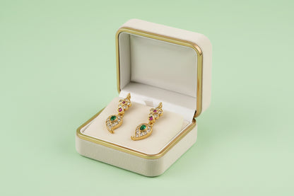 Gold earrings with gemstones in a jewelry box on a light green background